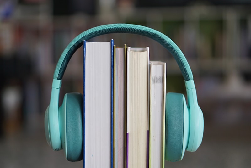 soft focus of the books stacked up with teal headphones on. There is a bookshelf in the background.