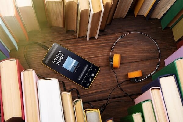 soft focus of the books stacked up with teal headphones on. There is a bookshelf in the background.