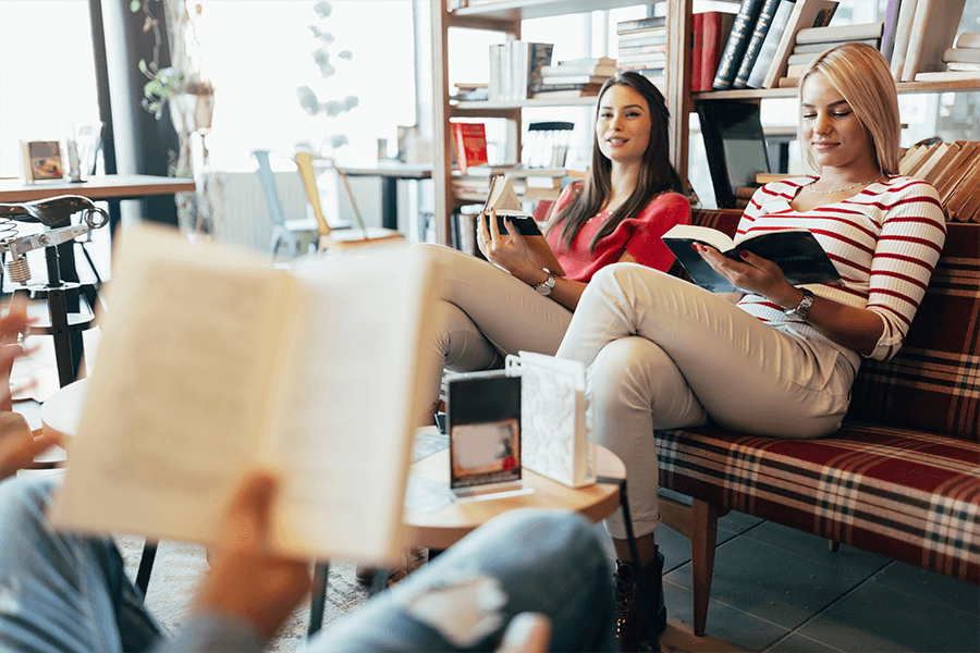 Three friends sitting on couches in a library cafe reading books together