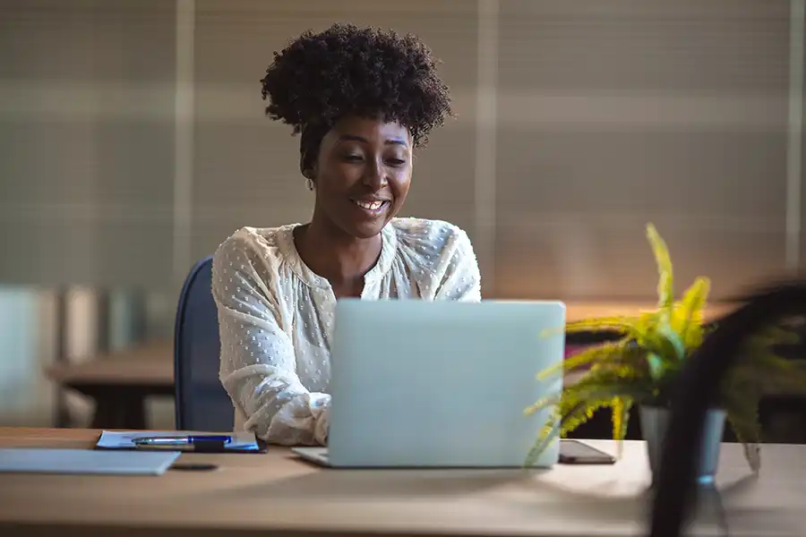 A young woman author wearing a white blouse typing on her laptop while sitting in an office